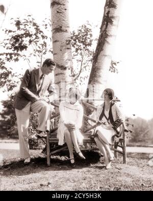 1920s MAN TWO WOMEN FASHIONABLE UPSCALE GROUP SITTING TALKING TOGETHER ON RUSTIC BENCH BY BIRCH TREE BERKSHIRE MOUNTAINS MA USA - r4096 HAR001 HARS PAIR ROMANCE BEAUTY COMMUNITY SUBURBAN SPRING OLD TIME NOSTALGIA OLD FASHION 1 STYLE MOUNTAINS WEALTHY COMPETITION VACATION FASHIONABLE RICH JOY LIFESTYLE FEMALES MARRIED RURAL SPOUSE HUSBANDS HEALTHINESS LUXURY UNITED STATES COPY SPACE FRIENDSHIP FULL-LENGTH LADIES PERSONS UNITED STATES OF AMERICA MALES CONFIDENCE BERKSHIRE B&W PARTNER NORTH AMERICA MASSACHUSETTS NORTH AMERICAN TIME OFF HAPPINESS RUSTIC WELLNESS STYLES TRIP GETAWAY RECREATION Stock Photo