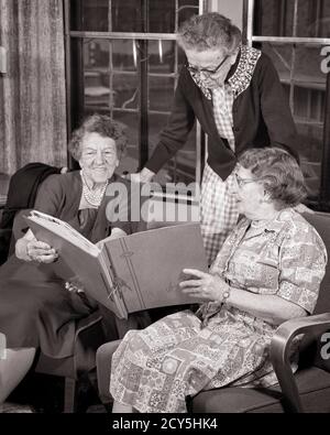 1960s THREE SENIOR WOMEN STANDING SITTING SIDE BY SIDE READING SHARING A MEMORY SCRAPBOOK PHOTO ALBUM IN RETIREMENT HOME - s15919 HAR001 HARS COMMUNICATION FRIEND PLEASED FAMILIES JOY LIFESTYLE MEMORY SATISFACTION ELDER FEMALES HOME LIFE SCRAPBOOK COPY SPACE FRIENDSHIP HALF-LENGTH LADIES PERSONS RETIREMENT SIBLINGS SISTERS SENIOR ADULT B&W SENIOR WOMAN RETIREE HAPPINESS OLD AGE OLDSTERS CHEERFUL OLDSTER LEISURE AGING EXCITEMENT REMEMBER PRIDE A IN SIBLING SMILES ELDERS CONNECTION CONCEPTUAL FRIENDLY JOYFUL AGISM COOPERATION ELDERLY WOMAN MEMORIES SIDE BY SIDE TOGETHERNESS BLACK AND WHITE Stock Photo