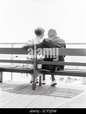 1970s BACK VIEW AFFECTIONATE SENIOR RETIRED COUPLE SITTING ON SEASIDE BOARDWALK BENCH LOOKING AT BEACH AND OCEAN NEW JERSEY USA - s19670 HAR001 HARS ELDER FEMALES MARRIED SPOUSE HUSBANDS COPY SPACE FRIENDSHIP HALF-LENGTH HUG LADIES PERSONS CARING MALES RETIREMENT SENIOR MAN EMBRACING SENIOR ADULT BOARDWALK B&W PARTNER SENIOR WOMAN SHORE RETIREE OLD AGE OLDSTERS OLDSTER BEACHES ELDERS CONNECTION CONCEPTUAL AFFECTIONATE SANDY ELDERLY MAN PERSONAL ATTACHMENT AFFECTION COOPERATION ELDERLY WOMAN EMOTION TOGETHERNESS WIVES BLACK AND WHITE CAUCASIAN ETHNICITY COASTAL HAR001 OLD FASHIONED Stock Photo
