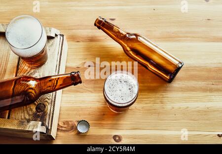 Two empty beer bottles, two glasses with beer and a bottle cap on a wooden background, top view Stock Photo