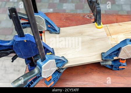Joining wooden handmade box with clamps joiners after glueing. Different chisels, drills and pencils at craftsman workshop. DIY instruments on wood Stock Photo