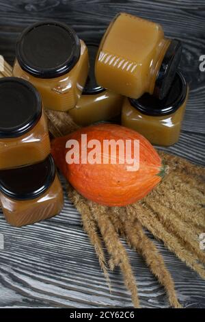 Jam in jars. Nearby is a pumpkin and a bouquet of dry grass with spikelets. On black pine boards. Stock Photo