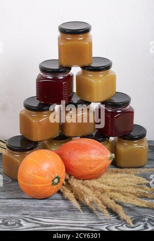 Jam in jars. Nearby is a pumpkin and a bouquet of dry grass with spikelets. On black pine boards. Stock Photo