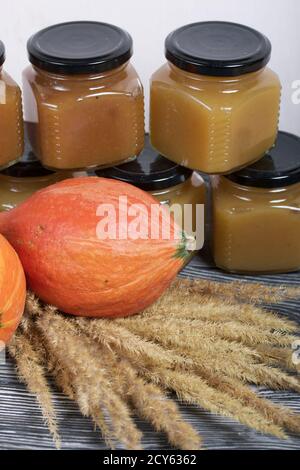 Jam in jars. Nearby is a pumpkin and a bouquet of dry grass with spikelets. On black pine boards. Stock Photo