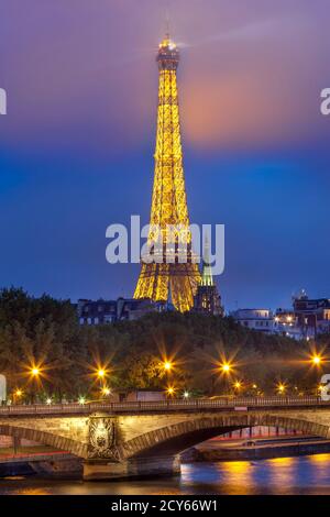 Foggy mist surrounding the top of the Eiffel Tower at dusk with Pont des Invalides over River Seine below, Paris, France Stock Photo