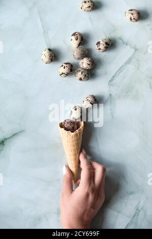 Easter flat lay with quail eggs flying out of waffle ice cream cone in hand. Top view on green stone table. Springtime trendy minimal greeting card Stock Photo