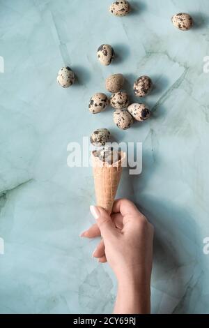 Easter flat lay with quail eggs flying out of waffle ice cream cone in hand. Top view on green stone table. Springtime trendy minimal greeting card Stock Photo
