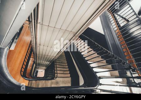 Wide-angle view from above of a long stairwell going down in a spiral in an old dwelling house with a metal railing and a lift shaft in the center, se Stock Photo