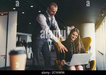 Two lauging business partners are discussing a new project design while having meeting in a modern office coworking area: man entrepreneur is pointing Stock Photo