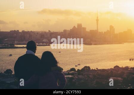 Happy senior couple watching sunset in Auckland city skyline with city center and Auckland Sky Tower in New Zealand. Stock Photo