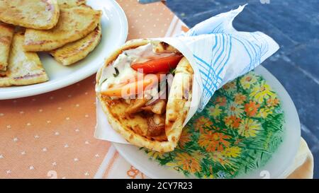 A wrapped gyro with chicken, tomato and yogurt alongside a plate of bread or pita at a cafe table in Rhodes Greece. Stock Photo