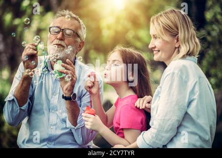 Happy family blows soap bubbles together while going vacation on weekend in the garden park in summer. Kid education and family activities concept. Stock Photo