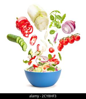 Vegetable salad in levitation. Fresh vegetarian salad of cucumbers, cabbage, cherry tomatoes, onions, peppers, spinach and arugula. Flying pieces of salad over a blue saucer isolated on white. Stock Photo