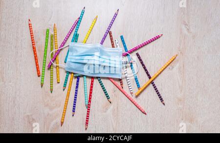 Top view of colored pencils scattered on a school table under a mask. Back to School in Pandemic Time, School Covid Protection-19 Stock Photo
