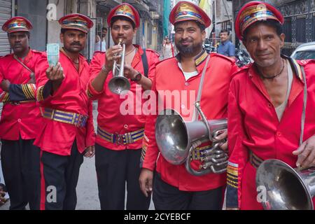 Five red-uniformed members of an Indian wedding and festival band in Mumbai, India, the second musician from left holding up part of his meagre pay Stock Photo