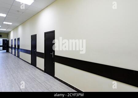empty corridor in the modern office building. There are many brown doors along a very long corridor with beige walls. Stock Photo