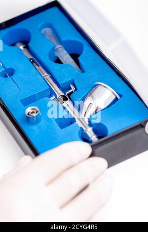Close up shot of manicure master hand is taking out new clean airbrush tool for nails wearing gloves from the blue box Stock Photo