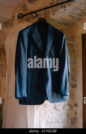 Blue jacket of the groom on a black hanger with a white cover for clothes in the room. Stock Photo