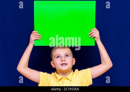 Portrait of joyful schoolboy posing with blank banner against studio blue background. Advertising concept.advertising shows overhead Stock Photo