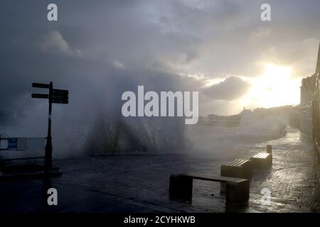 The sun rises behind the clouds as waves crash along the coast at Swanage in Dorset. Parts of the UK are preparing to be lashed by heavy rain and high winds as Storm Alex heralds the arrival of a stretch of bad weather over the weekend. Stock Photo