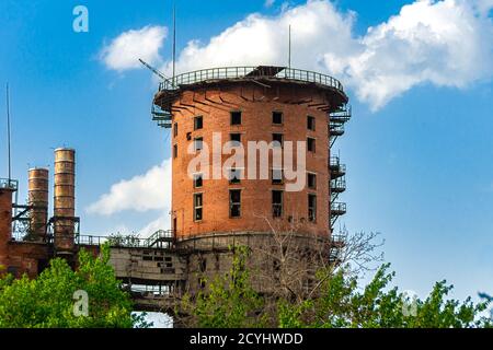 abandoned industrial building made of brick, round in shape, with a ruined overpass against blue sky with cumulus clouds Stock Photo