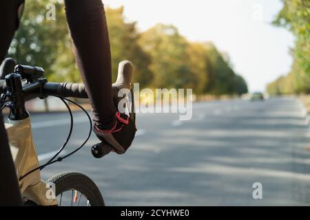 Hands of a cyclist resting on road bike handlebars, road view with copy space. Cycling, bicycle sport training outdoors Stock Photo