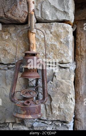 Old Rusty Oil Lamp Hanging on Rustic Wooden Hook in Stone Wall Stock Photo