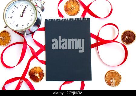 Bright festive red ribbon and curl and a notebook with black pages, slices of dried lemon and vintage silver alarm clock isolated on white background. Stock Photo