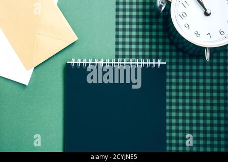 Open spiral notepad with black pages, white and beige envelopes and a beautiful vintage silver alarm clock on a green checkered background. List of go Stock Photo