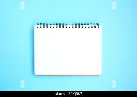 Open white notebook on a spiral on a bright blue background. Blank white notepad page. Blue set. Stationery on a blue background with space for text. Stock Photo