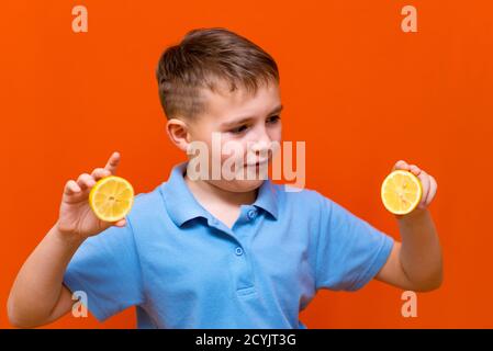 Close up Caucasian young child shows raw slices of lemon on a orange background. Healthy, lifestyle and a happy childhood concept. Stock Photo