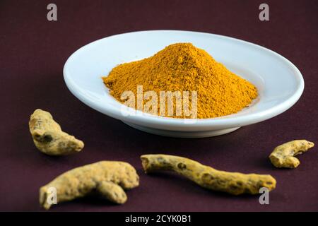close-up of a Pile of Turmeric powder in white plate and Turmeric sticks on red brown background. Macro shot, shallow depth of field. Stock Photo