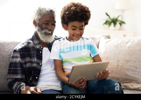 Senior man and grandson using digital tablet on couch at home Stock Photo