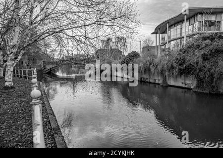 Black and white photo of the view from the waterside footpath along the River Wensum in the city of Norwich, Norfolk. The distant bridge is the White Friar's crossing. Stock Photo
