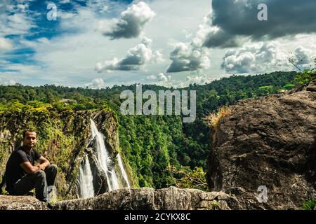 man siting at hilltop watching the beautiful waterfall at evening image is taken at jog fall karnataka india. it is showing the beauty of nature. Stock Photo