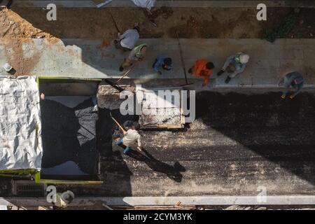 Construction workers on the road repair site unload the asphalt from the car manually.  Some workers rest in the shade.  Aerial view. Vietnam Stock Photo