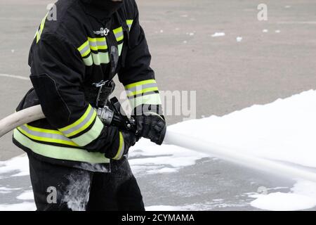 Feeding foam from the handheld fire fighter, fire extinguishing foam flies out of the trunk, which keeps the fireman in combat clothing Stock Photo