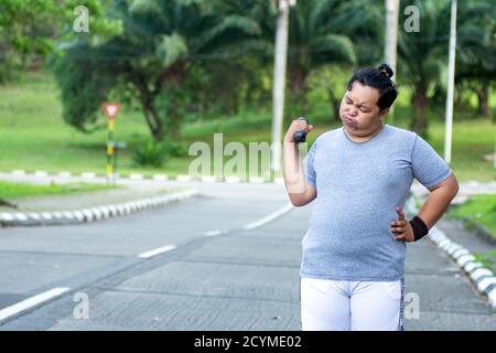 Asian young men with obesity trying to lose weight with barbell exercises and feel not strong in outdoor city parks Stock Photo