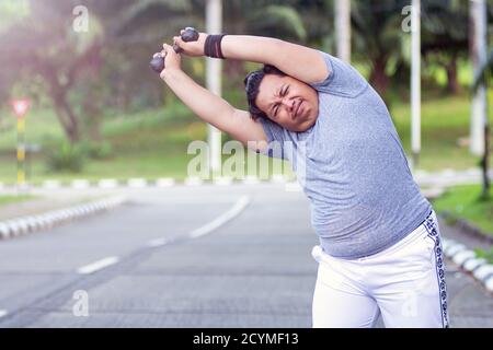 Asian young men with obesity trying to lose weight with barbell exercises and feel not strong in outdoor city parks Stock Photo