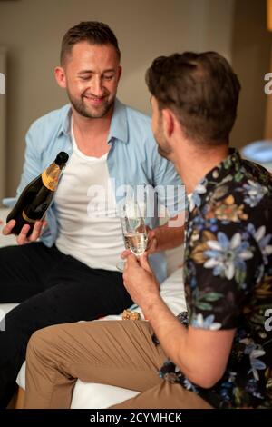 Two caucasian men drinking champagne, celebrating and having fun together on a hotel bed in Jesmond, England. Stock Photo