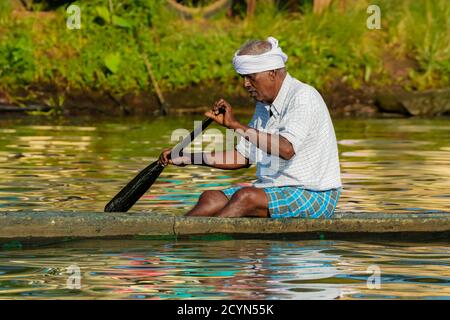 Old man paddling canoe in the backwaters region known for rice fields & houseboat cruises; Alappuzha (Alleppey), Kerala, India Stock Photo