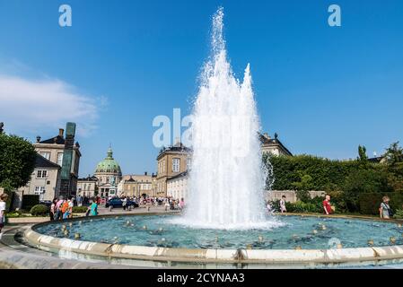 Copenhagen, Denmark - August 27, 2019: Fountain in the Garden of Amalienborg Palace and the Frederik Church (Frederiks Kirke) with people around in Co Stock Photo