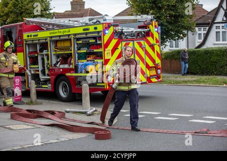 Woman Firefighter rolls out the hose with London Fire Brigade attending a house fire in a residential street, South London, England, United Kingdom