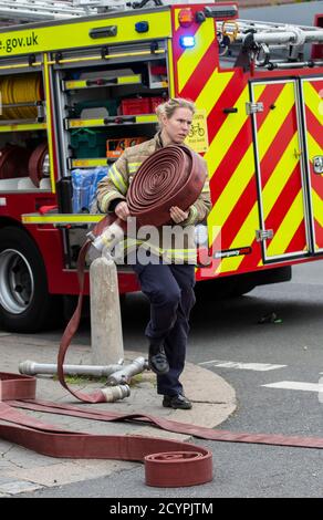 Woman Firefighter rolls out the hose with London Fire Brigade attending a house fire in a residential street, South London, England, United Kingdom