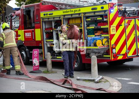Woman Firefighter rolls out the hose with London Fire Brigade attending a house fire in a residential street, South London, England, United Kingdom