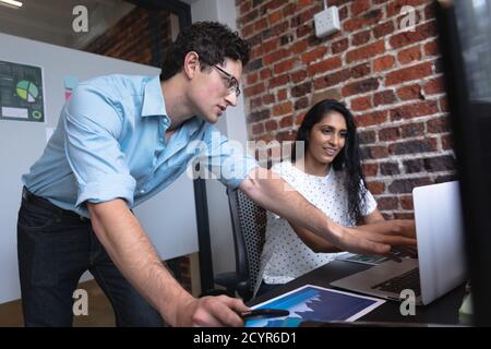 Mixed race woman and Caucasian man working in a casual office, using a laptop computer and discussing their work. Creative business professionals work Stock Photo