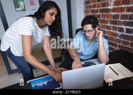 Mixed race woman and Caucasian man working in a casual office, using a laptop computer and discussing their work. Creative business professionals work Stock Photo