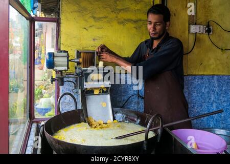 Man makes fried banana chips in deep fat fryer in shop on Main Road in this tea & coffee town in Wayanad district; Kalpetta, Wayanad, Kerala, India Stock Photo