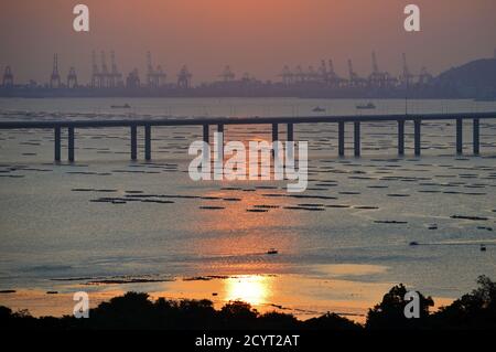 Shenzhen Bay Bridge crossing Deep Bay, between Hong Kong and Shenzhen, China, during sunset with Shekou container terminals in background Stock Photo