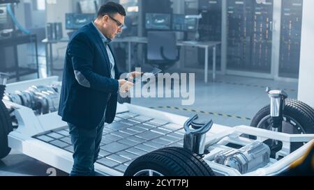 Automotive Design Engineer Looking at Technical Drawing of an Electric Car Chassis Prototype on a Tablet. In Innovation Laboratory Facility Concept Stock Photo